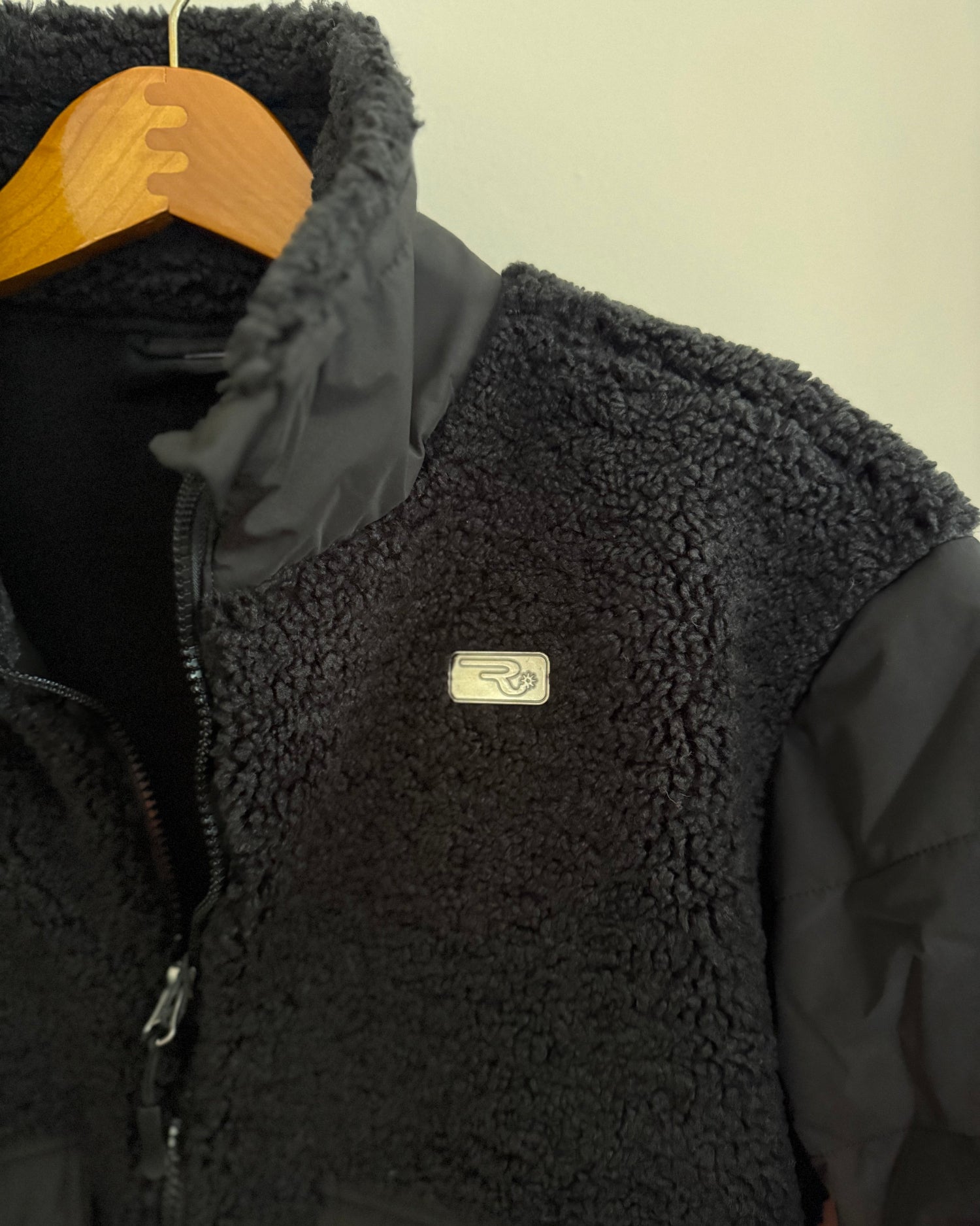 Black fleece vest with a brand logo on a hanger against a beige background