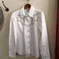 White shirt with lace details on a hanger against a beige wall.