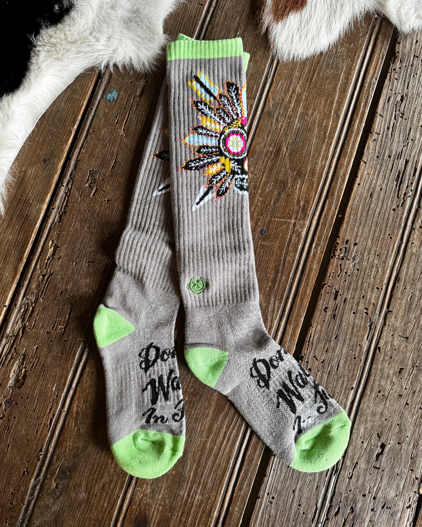 Gray socks with green accents and a colorful design on a wooden floor.