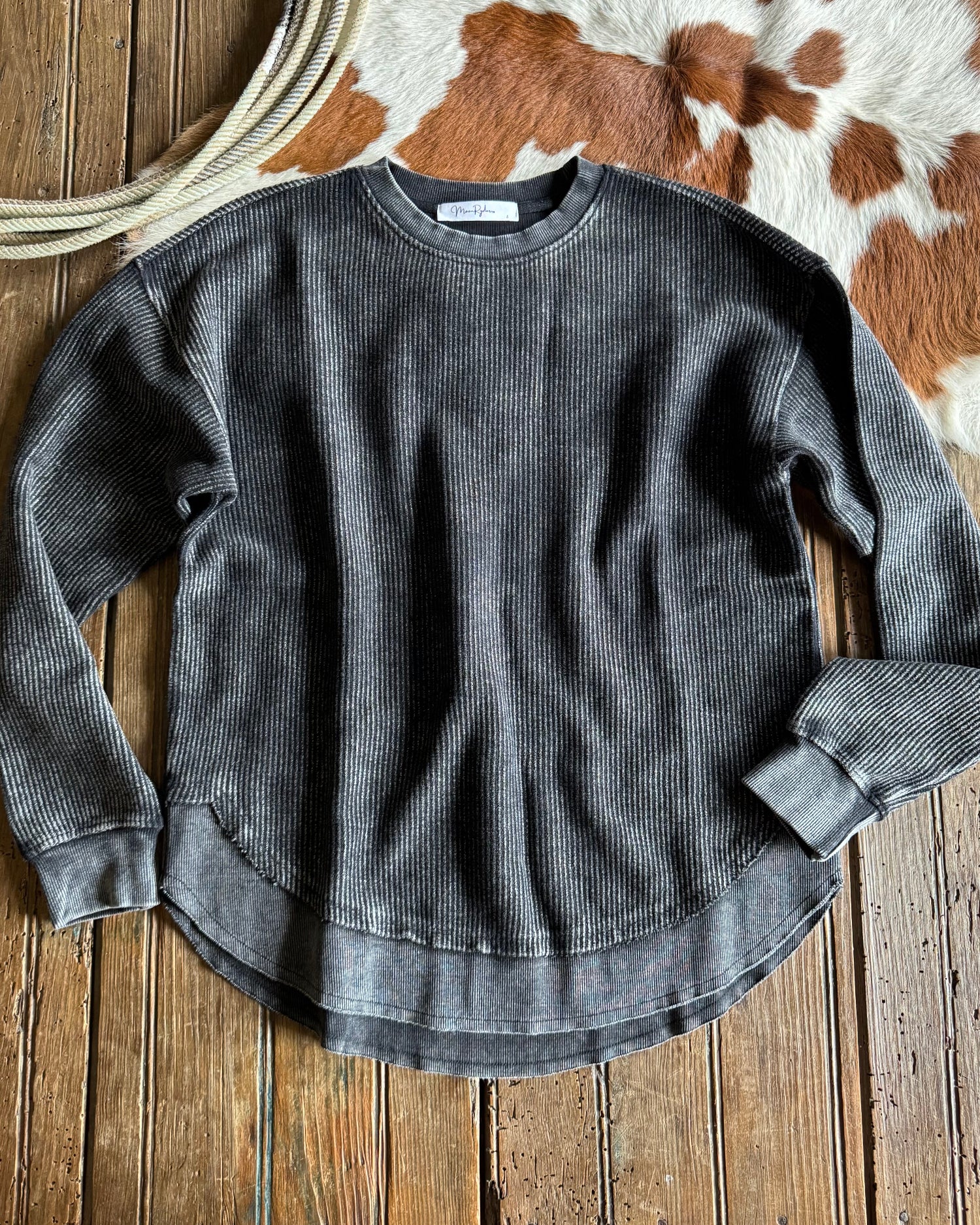 Gray ribbed sweater on a wooden surface with a cowhide rug in the background