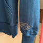 Blue sweatshirt with a logo on the sleeve against a beige background