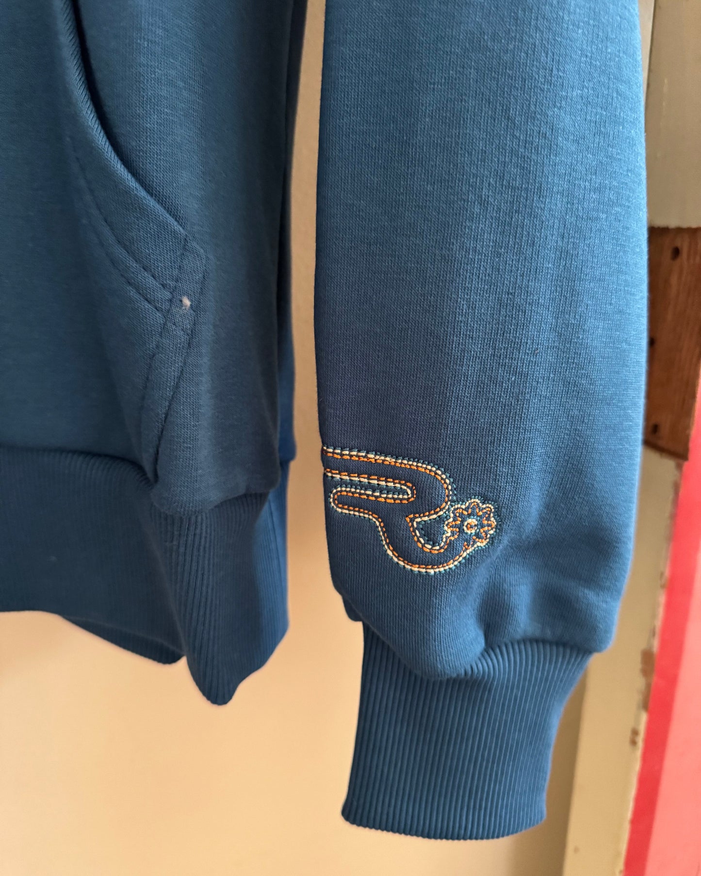 Blue sweatshirt with a logo on the sleeve against a beige background
