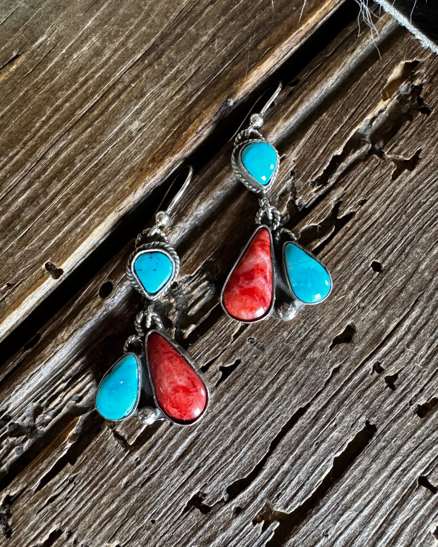Pair of earrings with turquoise and red stones on a wooden surface