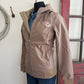 Brown jacket with a logo worn by a person, leaning against a wall.