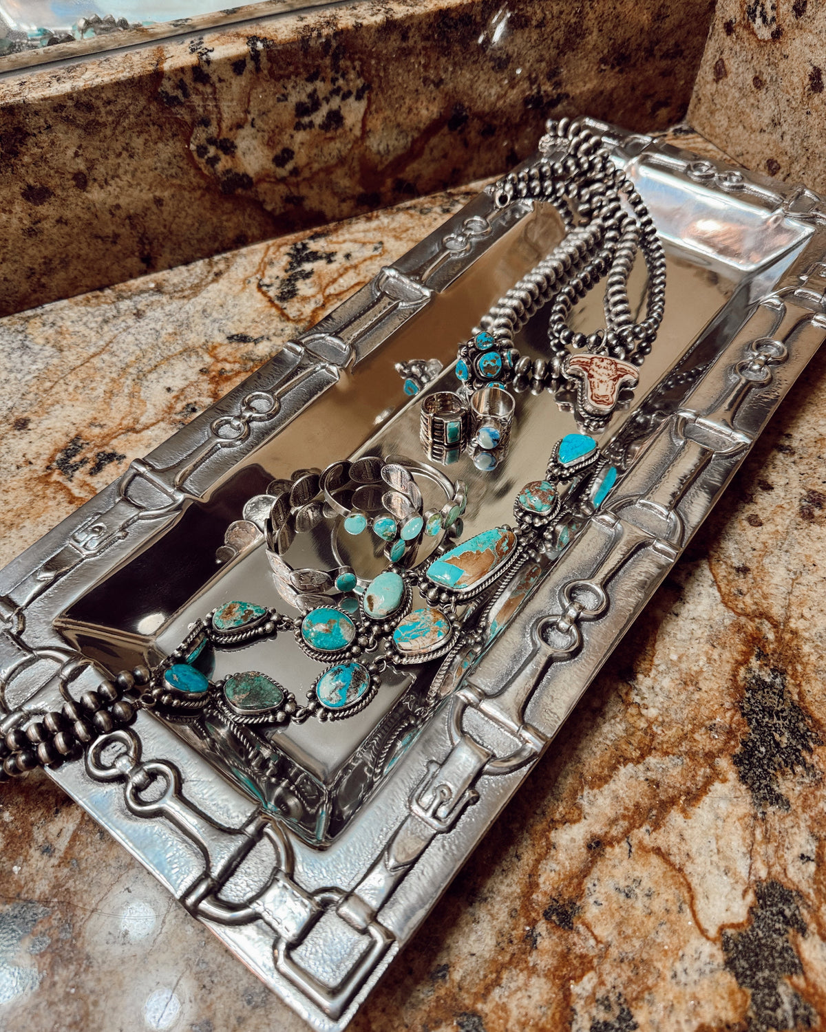 Silver jewelry set with turquoise stones on a decorative stand.