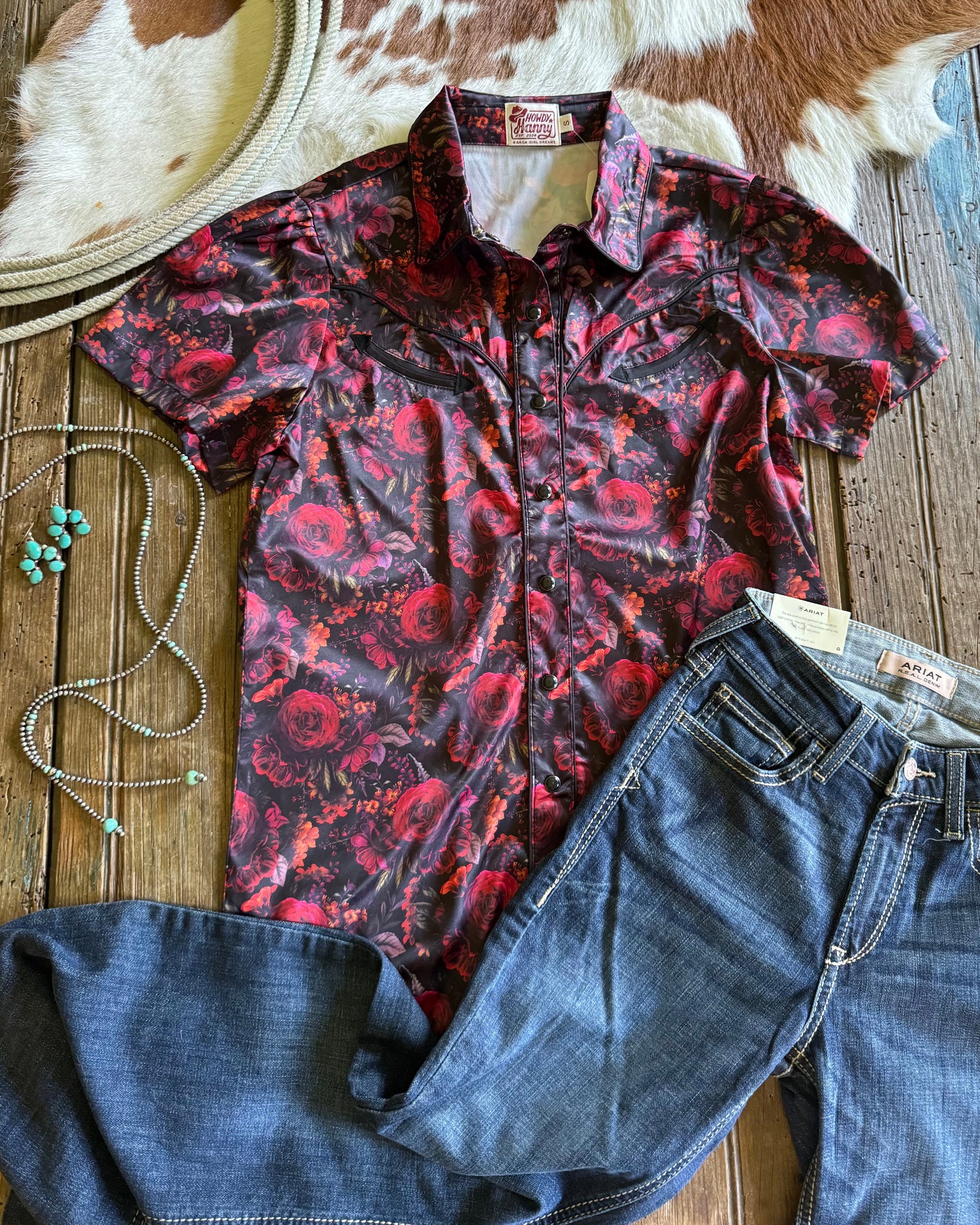 Red floral shirt and blue jeans on a wooden surface with a cowhide rug in the background.
