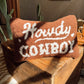 Decorative pillow with 'Howdy Cowboy' text on a wooden surface