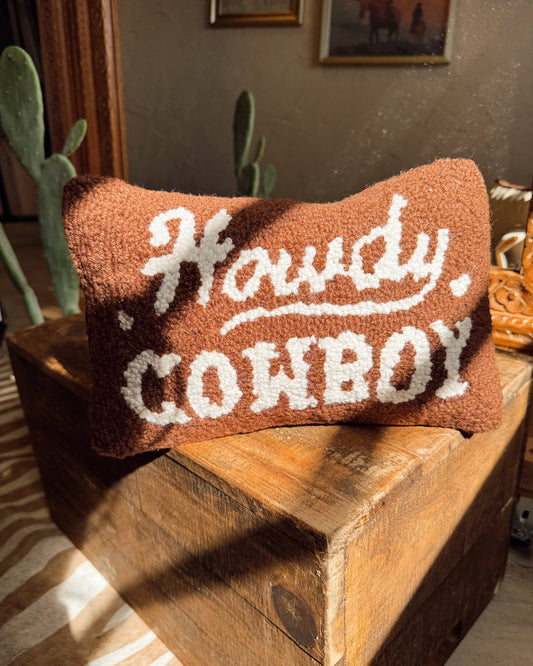 Decorative pillow with 'Howdy Cowboy' text on a wooden surface