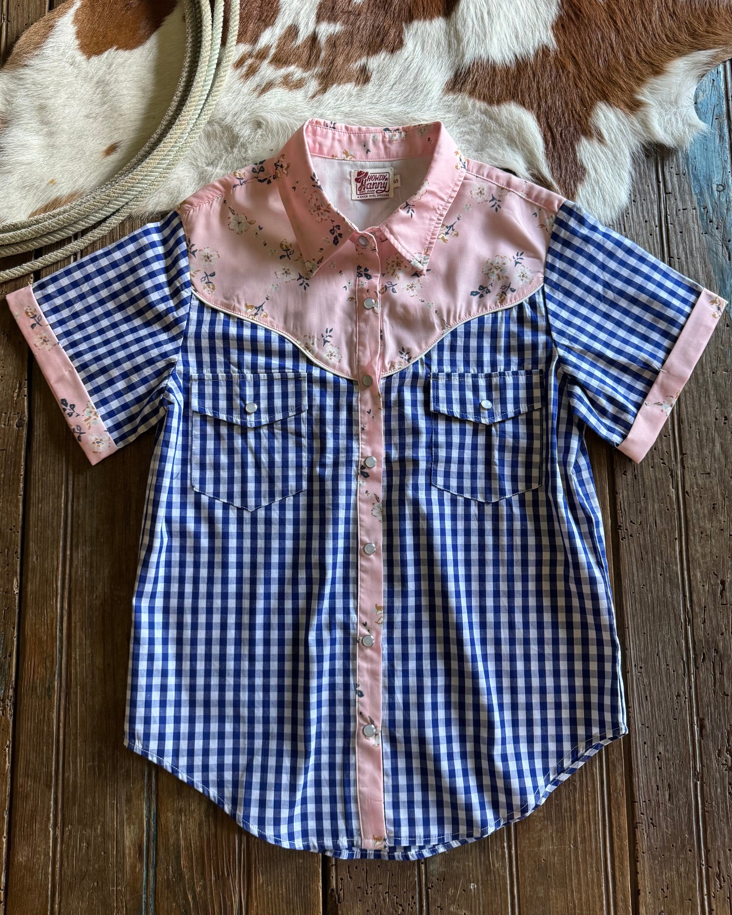 Blue checkered shirt with floral collar on a wooden surface with cowhide rug