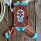 Colorful skull design sock on a wooden surface with cowhide rug and lasso.