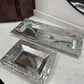 Two silver trays with decorative patterns on a marble surface.