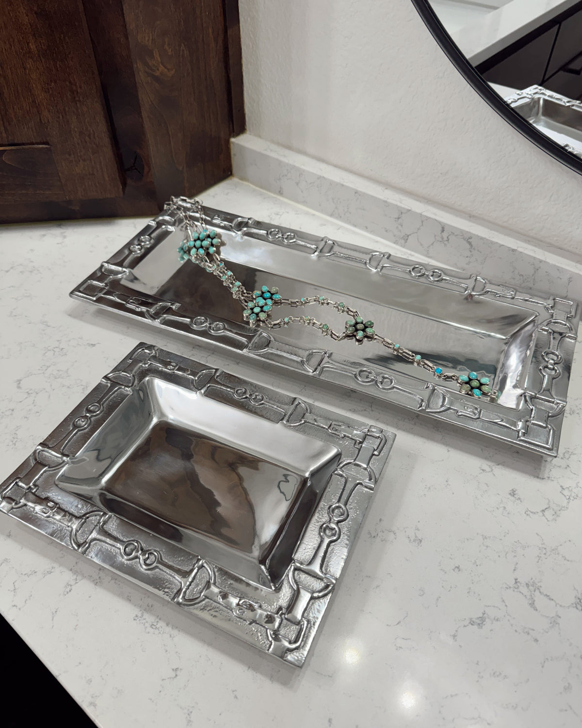 Two silver trays with decorative patterns on a marble surface.