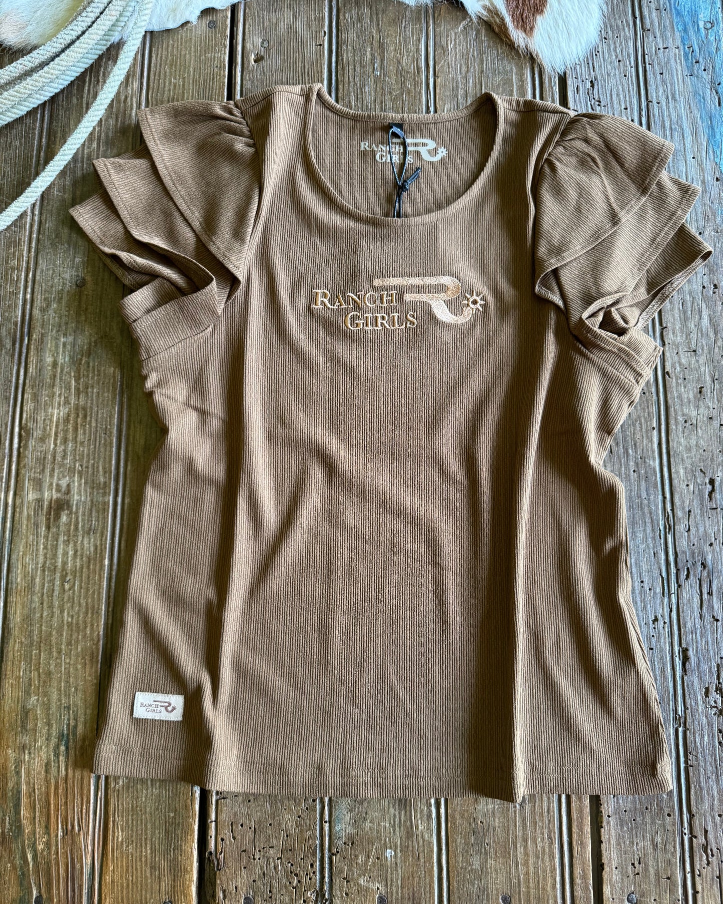 Beige tank top with 'Ranch Girls' logo on a wooden surface