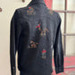 Black denim shirt with embroidered designs on a mannequin against a neutral wall.