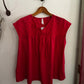 Red blouse with black detailing on a wooden hanger against a white wall.