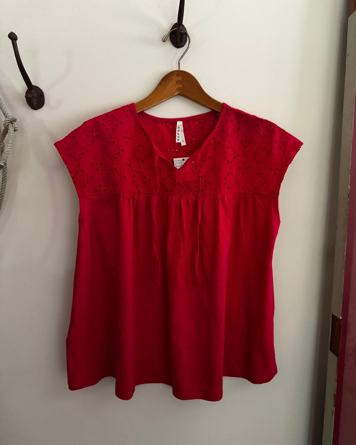 Red blouse with black detailing on a wooden hanger against a white wall.