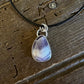 A teardrop-shaped amethyst pendant necklace with a silver bezel and black cord, displayed on a rustic wooden surface.