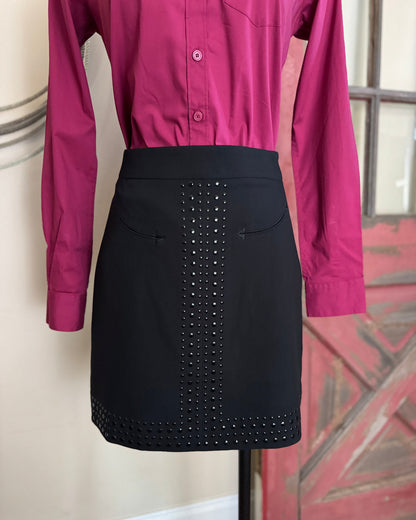 Black skirt with stud detailing worn over a magenta shirt on a mannequin against a neutral wall.