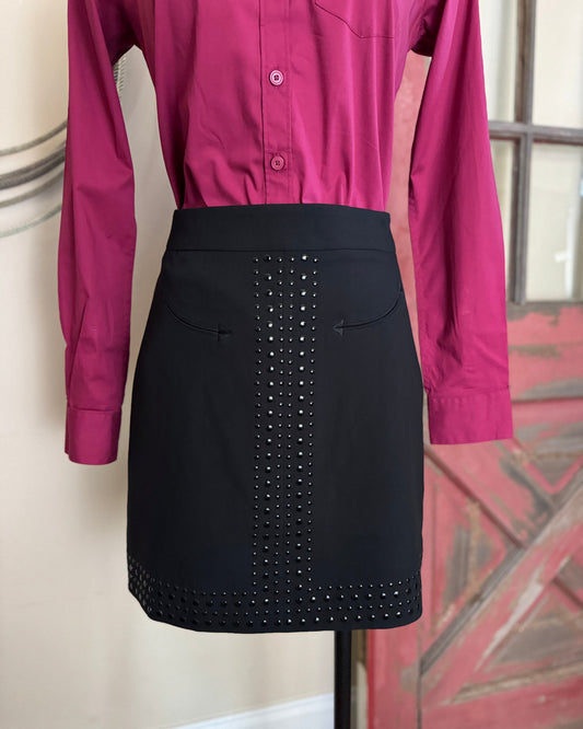 Black skirt with stud detailing worn over a magenta shirt on a mannequin against a neutral wall.