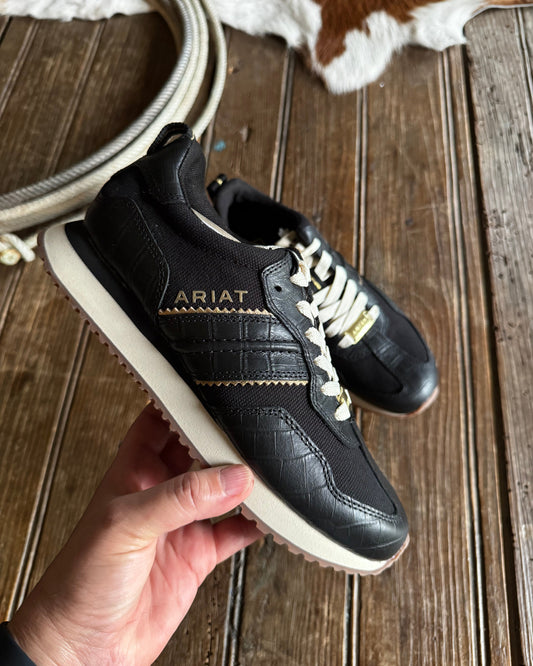 Black sneakers with white laces held by a hand on a wooden surface