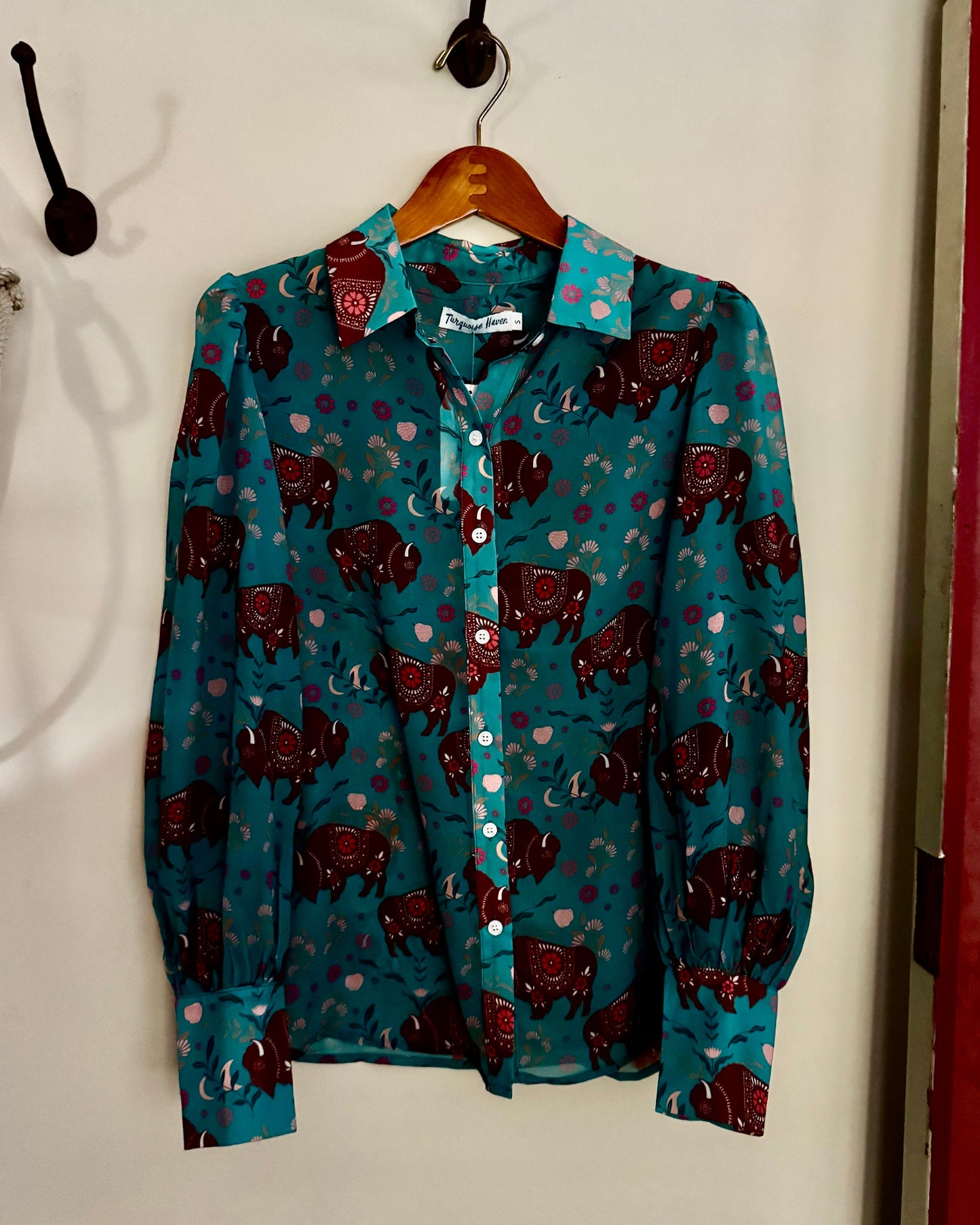 Teal shirt with red pattern on a hanger against a white wall