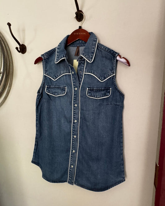 Folded denim shirt on a white surface with a fan and hook in the background