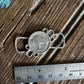 Silver pendant on a wooden surface with a ruler for scale
