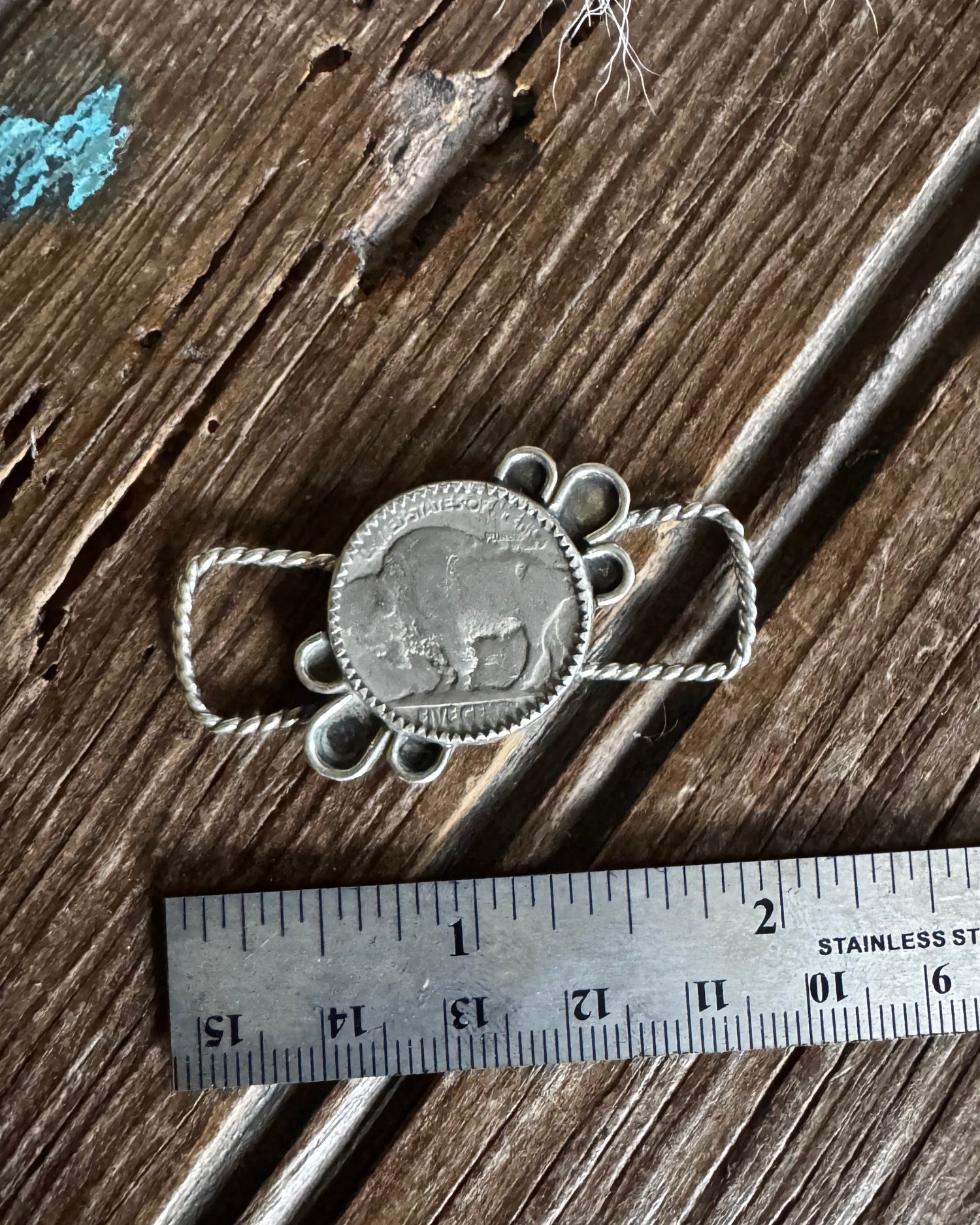 Silver pendant on a wooden surface with a ruler for scale