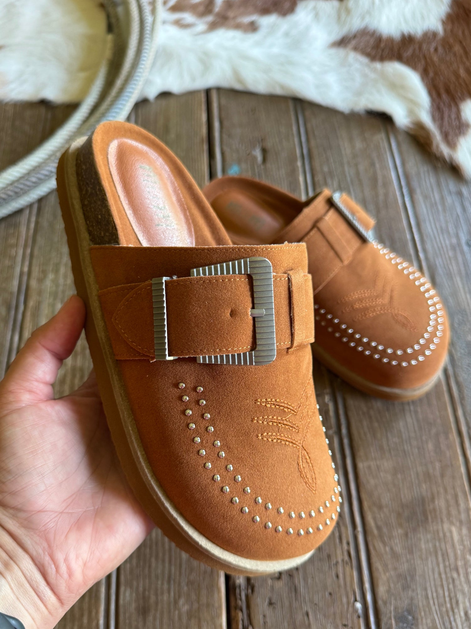 Brown shoes with a buckle held by a hand on a wooden surface.