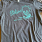 Gray t-shirt with teal 'Stetson Western Goods' logo on a wooden surface