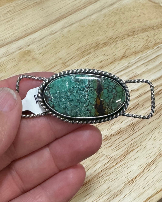Hand holding a green stone pendant on a wooden surface with a sink in the background