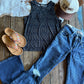 Blue jeans, black tank top, brown sandals, and a cap on a wooden surface with a cowhide rug.