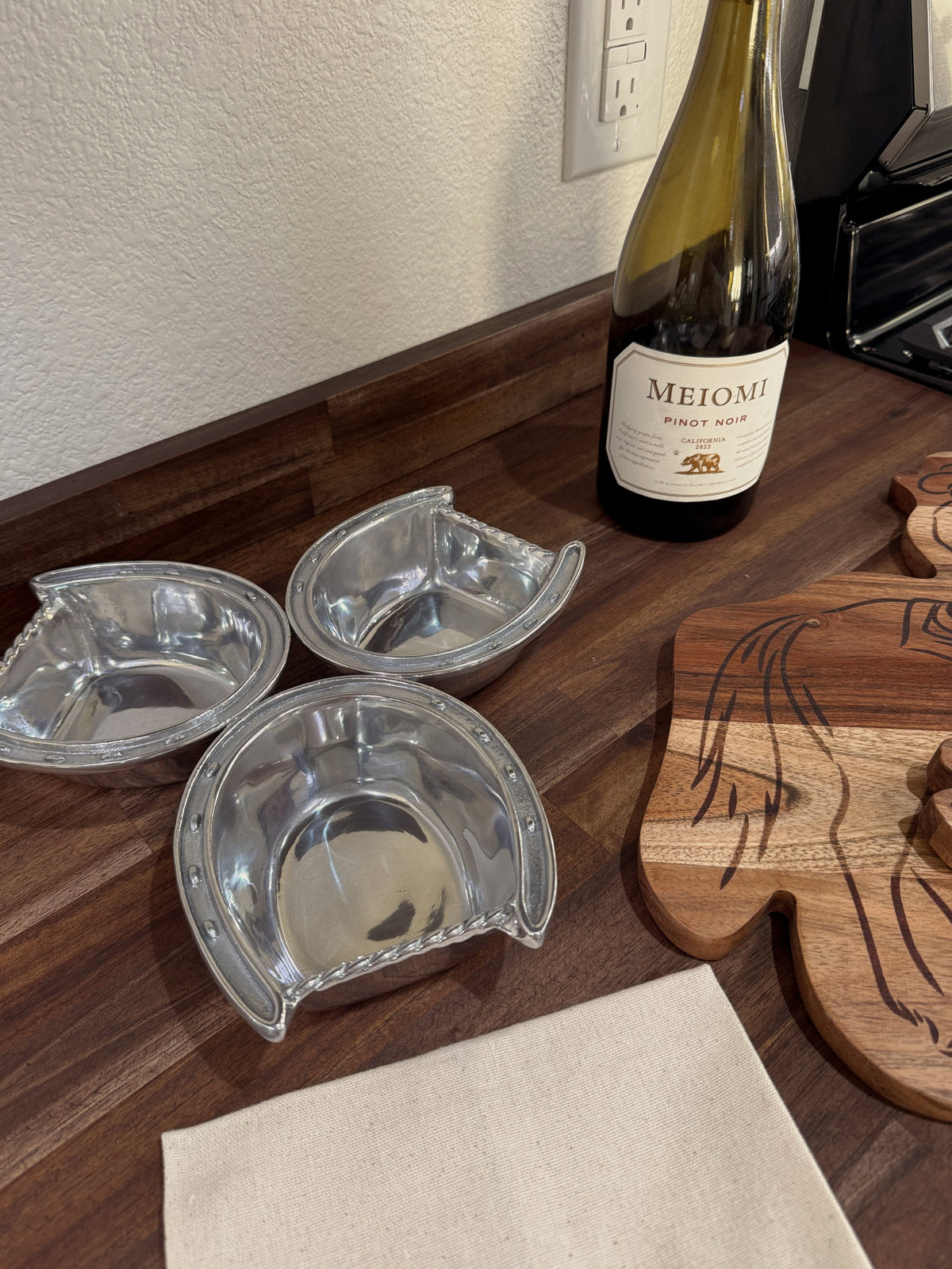 Three metal wine coasters on a wooden surface with a bottle of Meiji wine in the background.