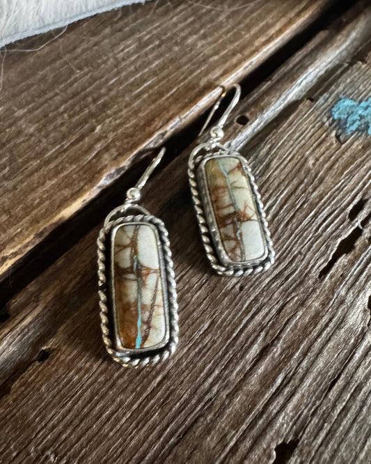 Pair of earrings with stone and silver setting on a wooden surface