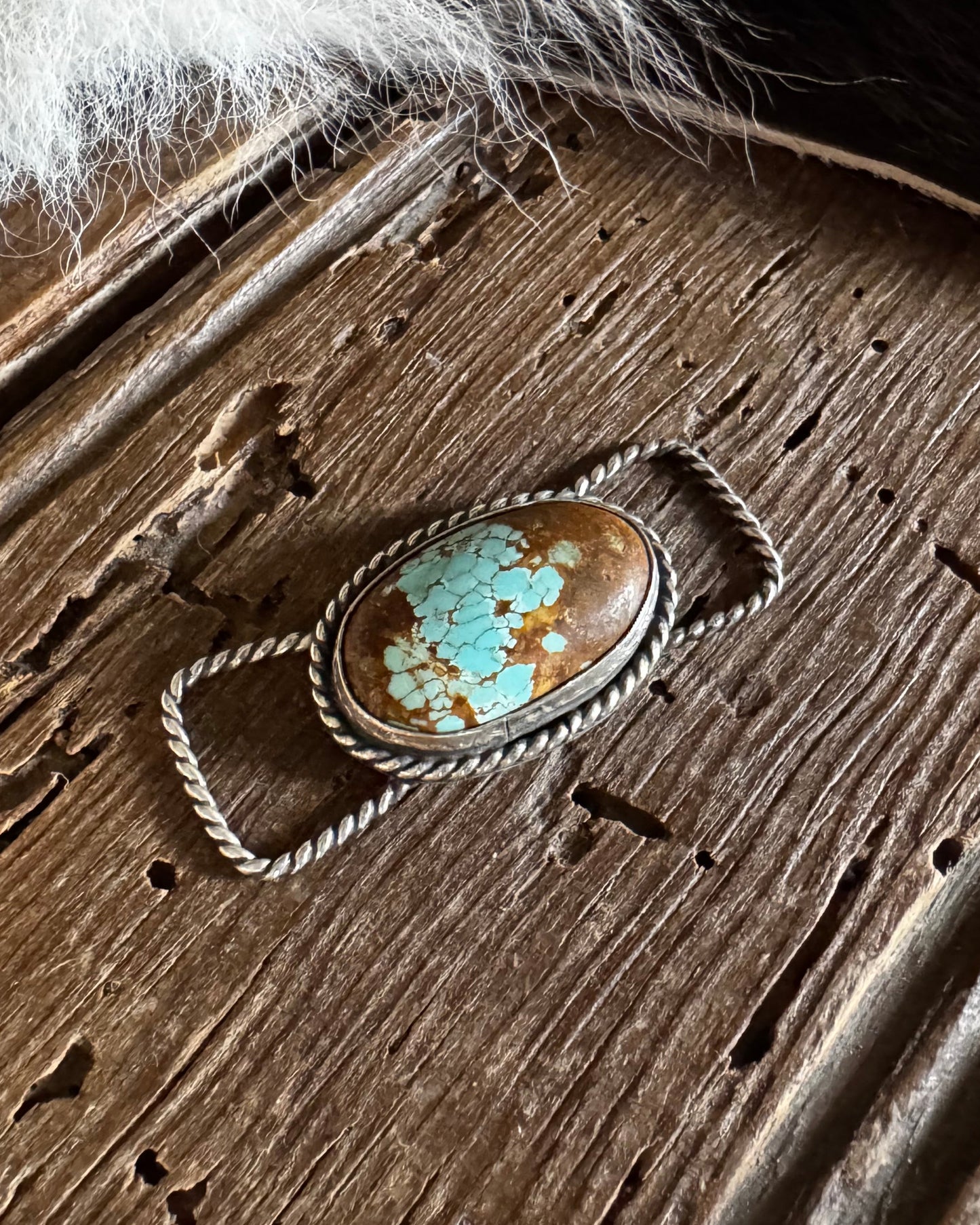 Turquoise stone pendant on a wooden surface with fur in the background
