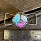 Necklace with a colorful stone pendant on a wooden surface with a ruler for scale.