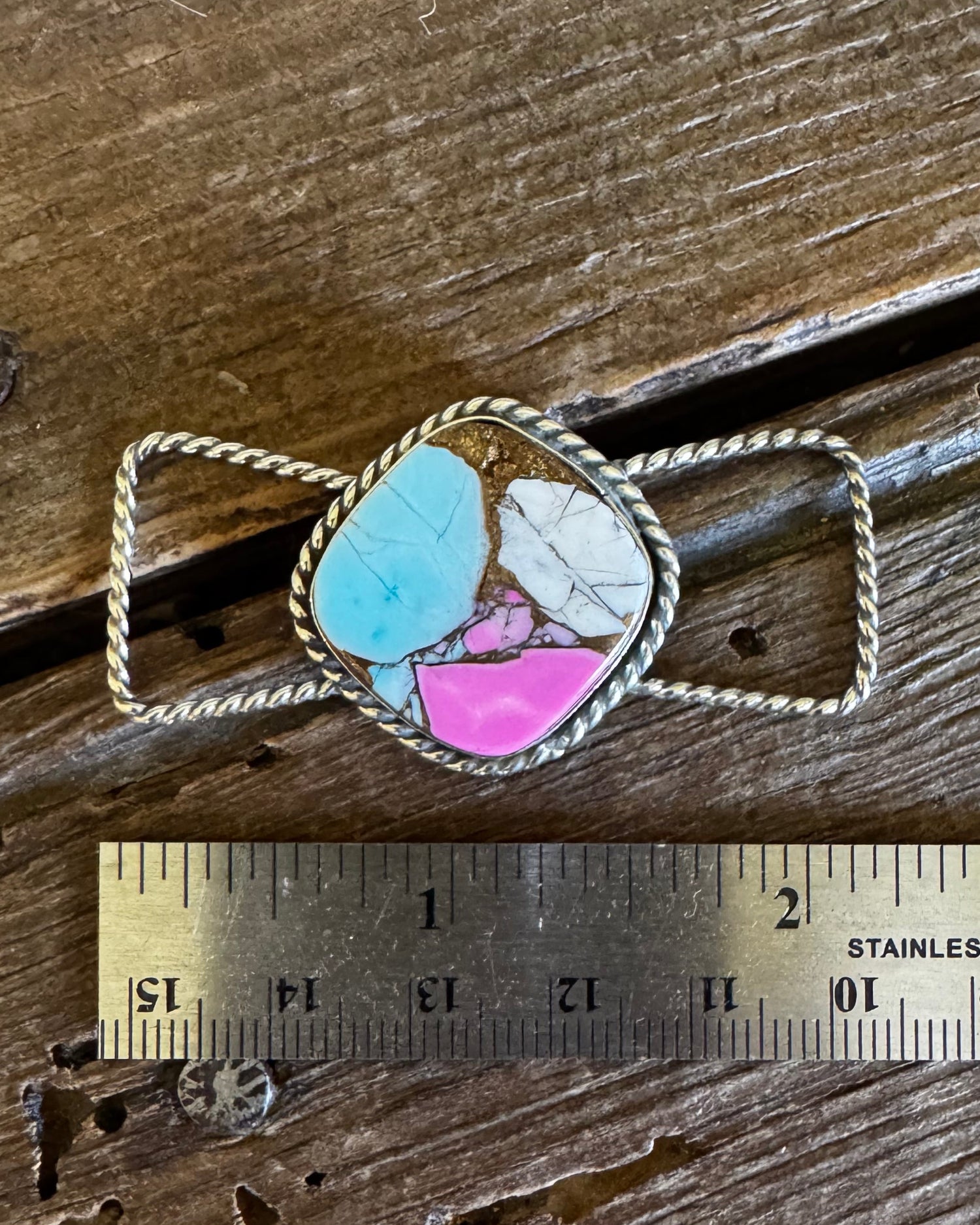 Necklace with a colorful stone pendant on a wooden surface with a ruler for scale.