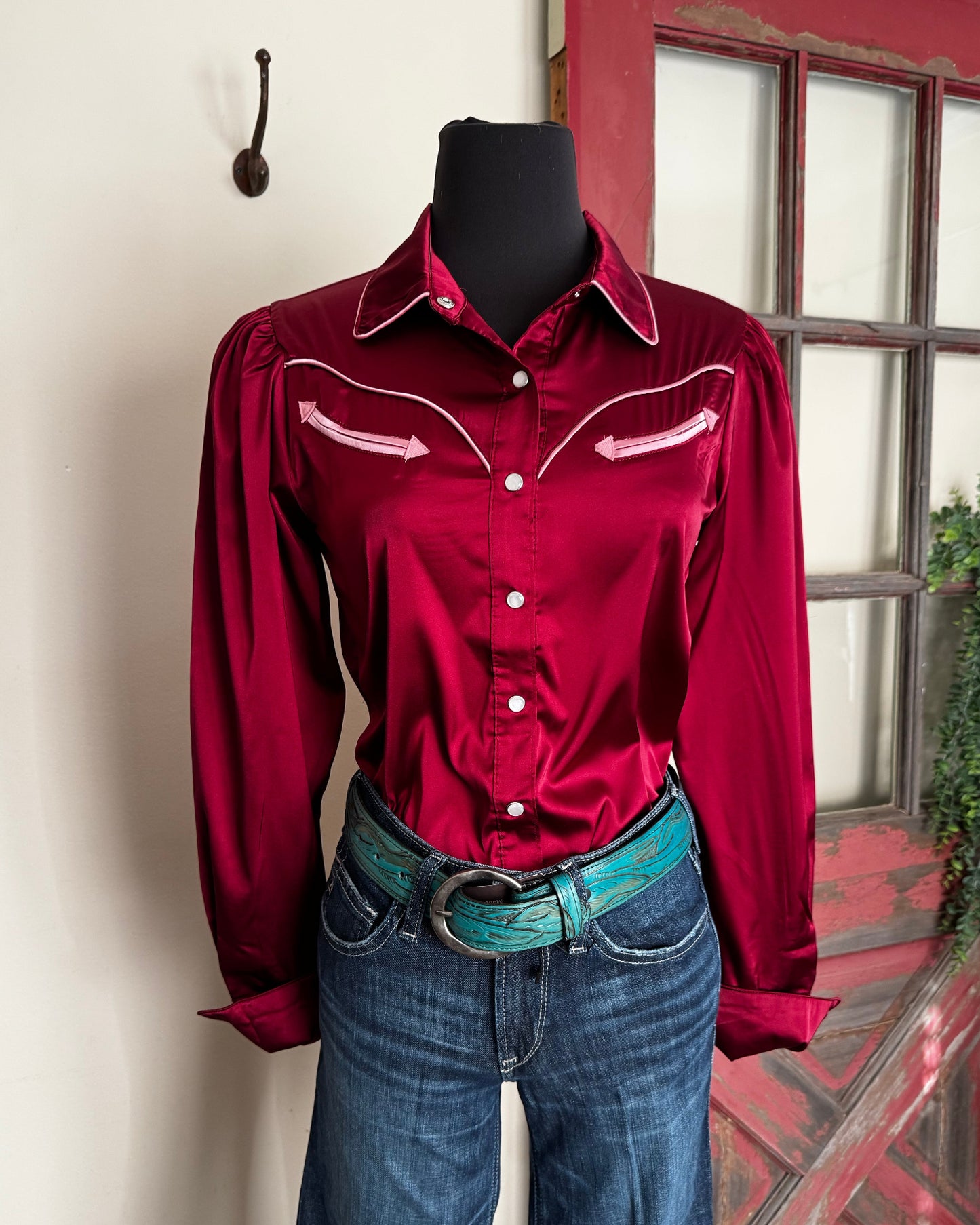 Red shirt with white buttons on a mannequin against a red door and white wall.