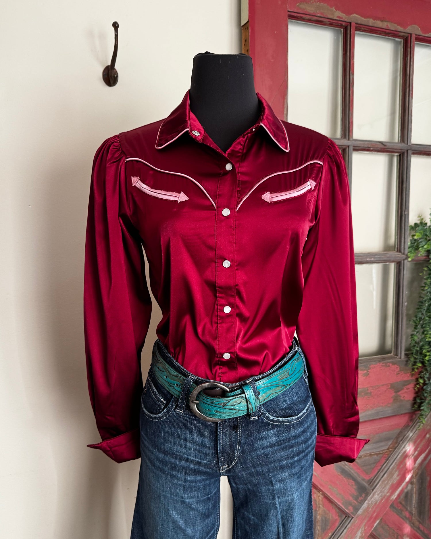 Red shirt with white buttons on a mannequin against a red door and white wall.