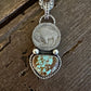A silver-toned necklace featuring a circular coin pendant and a heart-shaped turquoise stone pendant, displayed on a rustic dark wood surface.