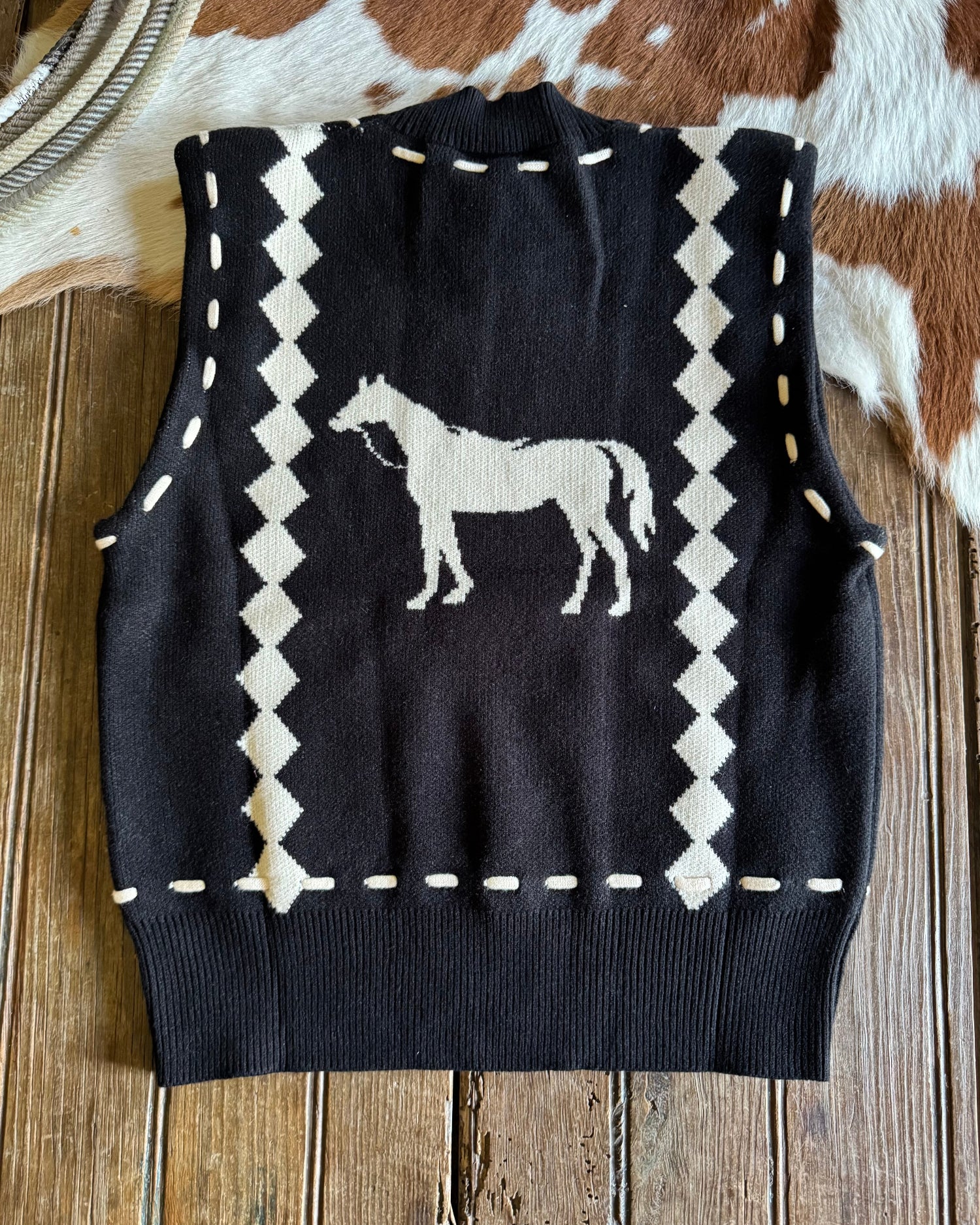 Black sweater vest with white horse design on a wooden surface