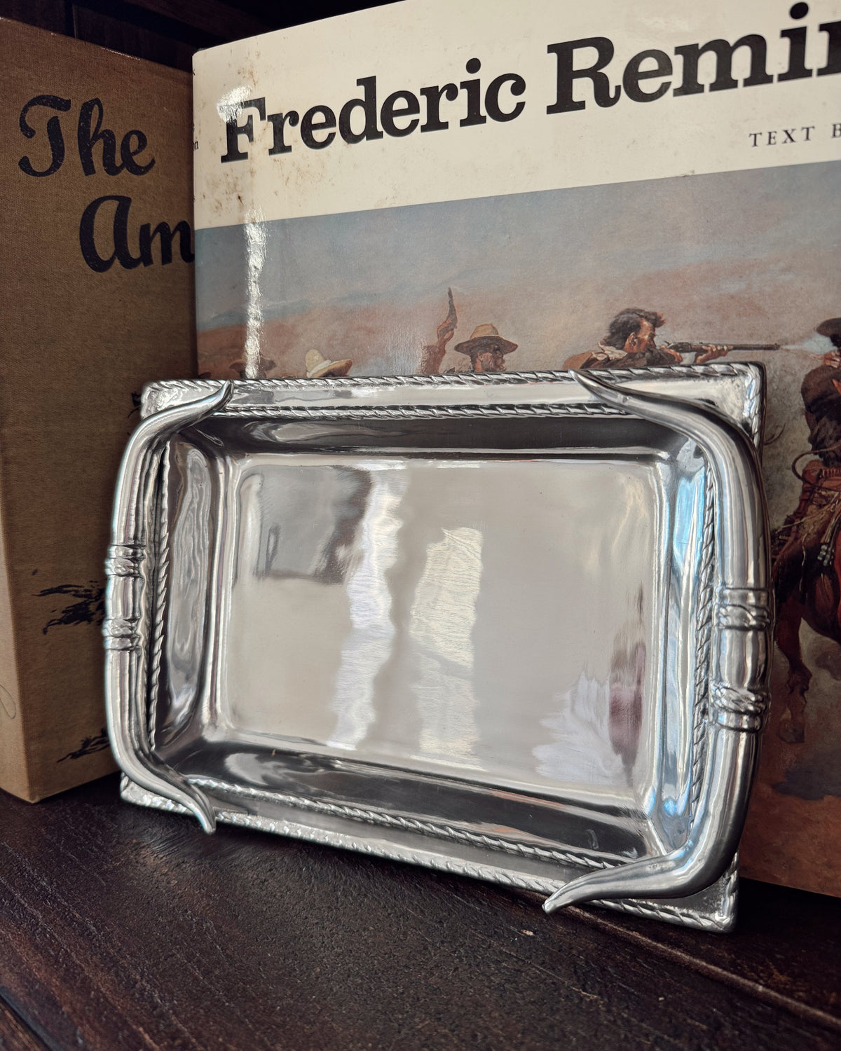 Silver tray on a wooden surface with a book titled 'Frederic Remington' in the background.