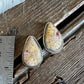 Two teardrop-shaped resin earrings with dried floral inclusions, displayed on a rustic wooden surface next to a metal ruler for scale.