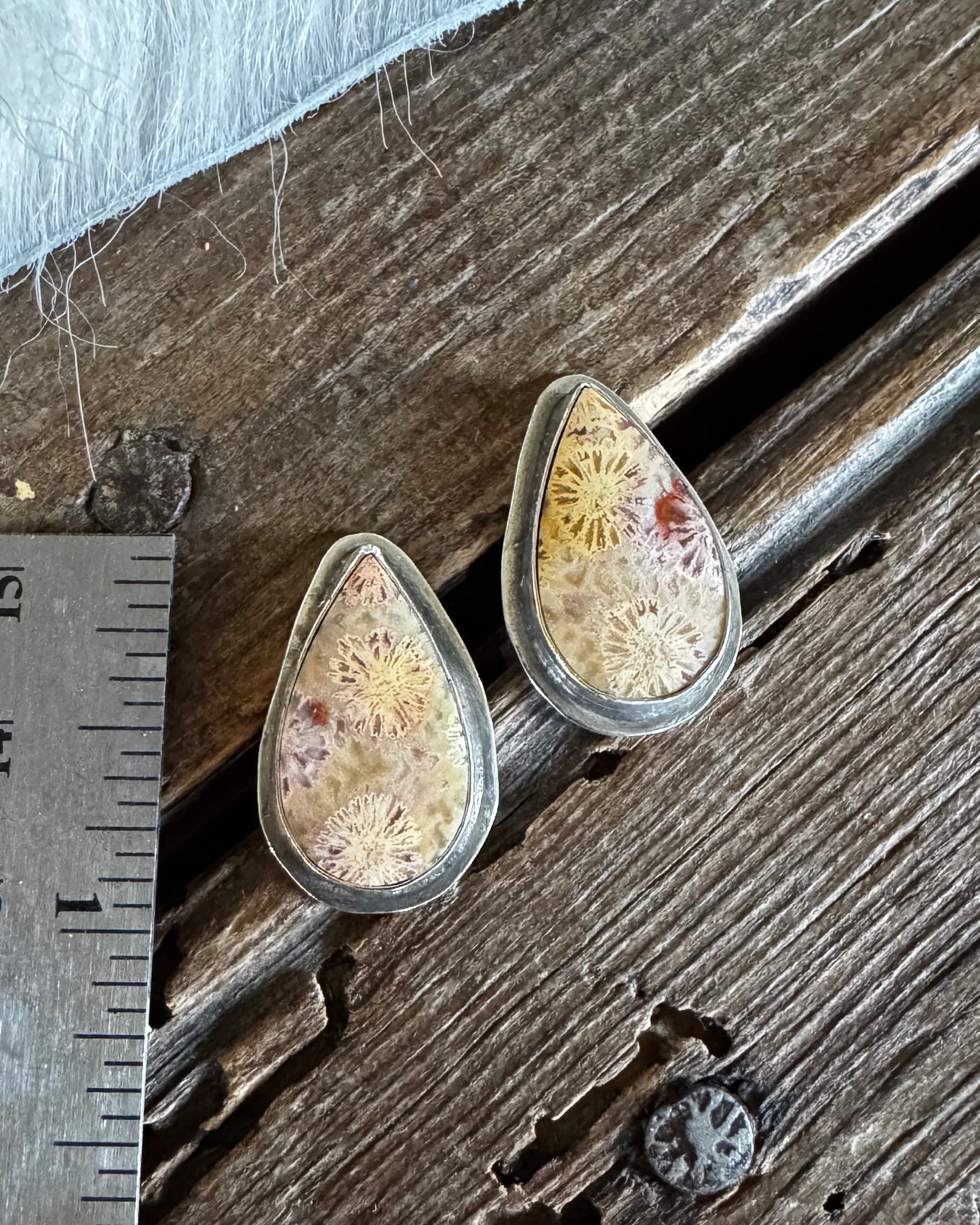 Two teardrop-shaped resin earrings with dried floral inclusions, displayed on a rustic wooden surface next to a metal ruler for scale.
