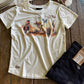 White t-shirt with graphic design and blue jeans on a wooden surface