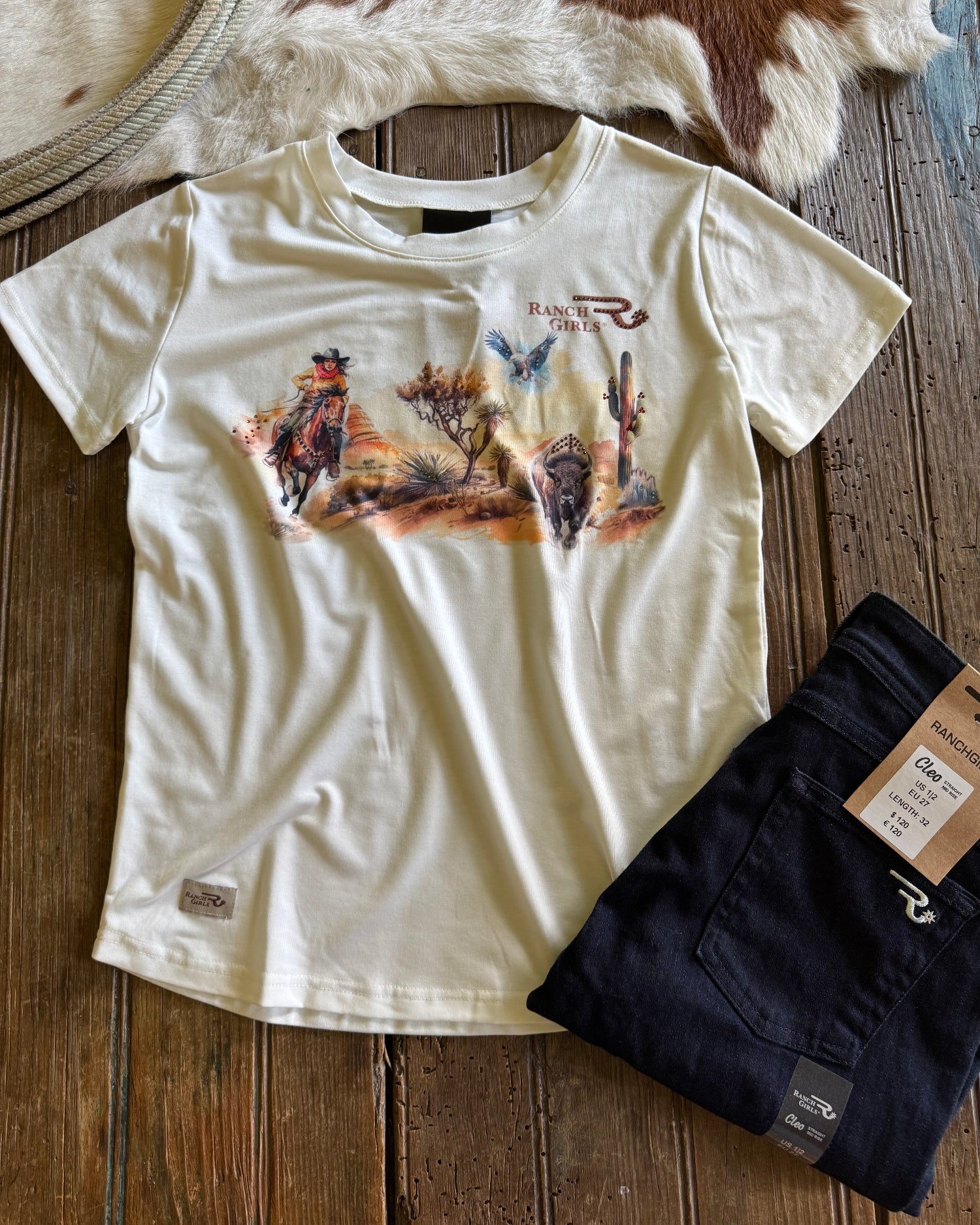 White t-shirt with graphic design and blue jeans on a wooden surface