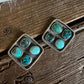 Pair of square earrings with turquoise stones on a wooden surface