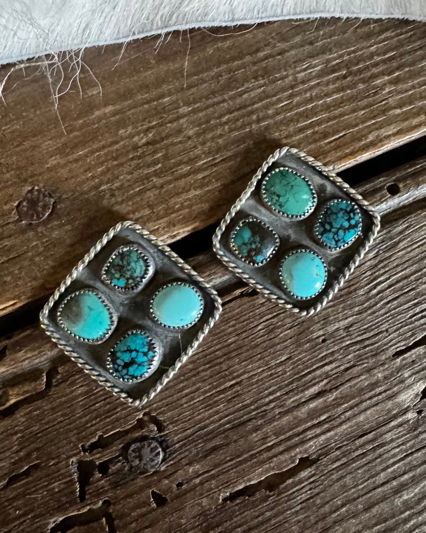 Pair of square earrings with turquoise stones on a wooden surface