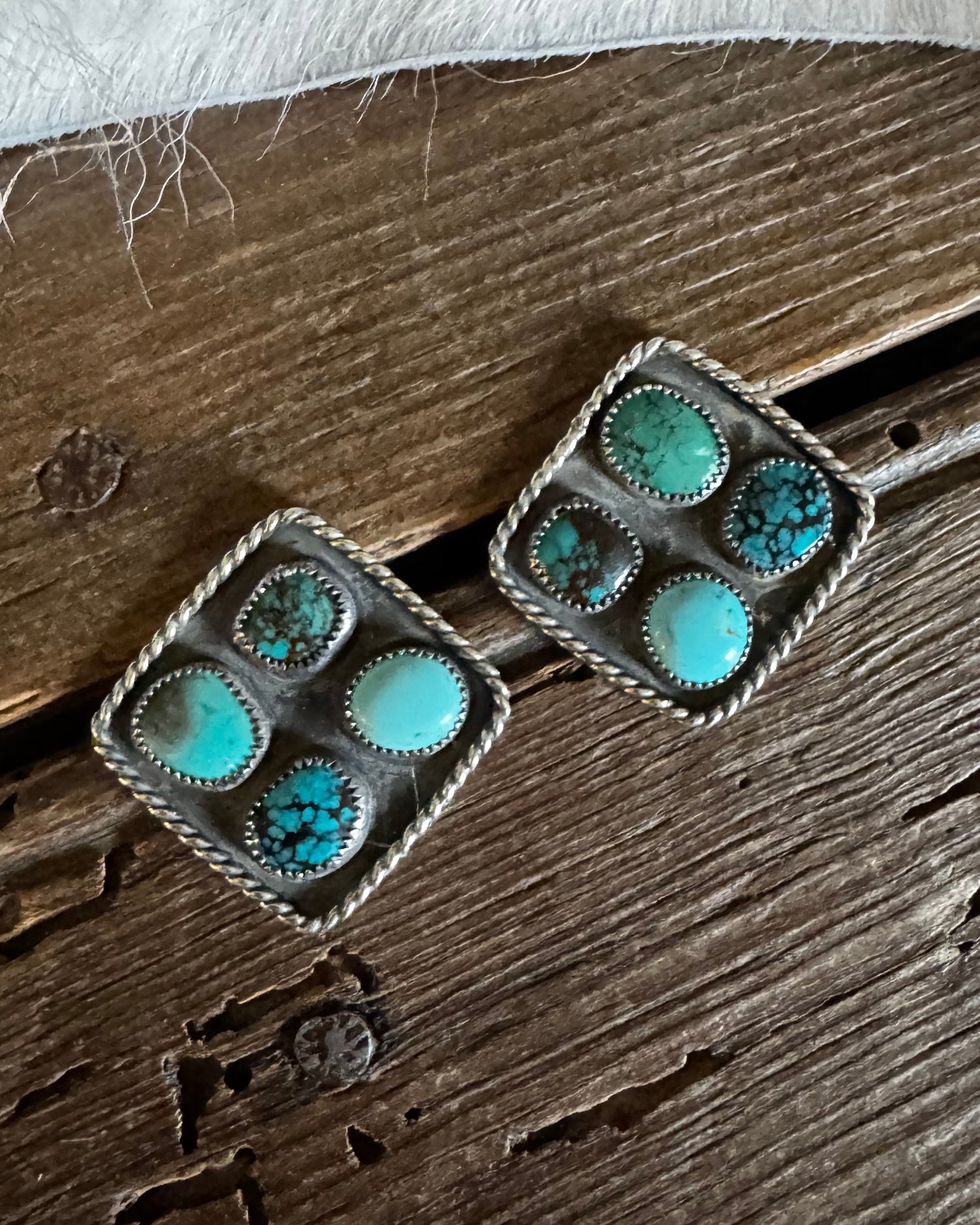Pair of square earrings with turquoise stones on a wooden surface
