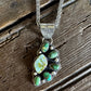 A silver-toned paw print pendant necklace with green turquoise-like stones and a white central stone, displayed on a rustic wooden surface.